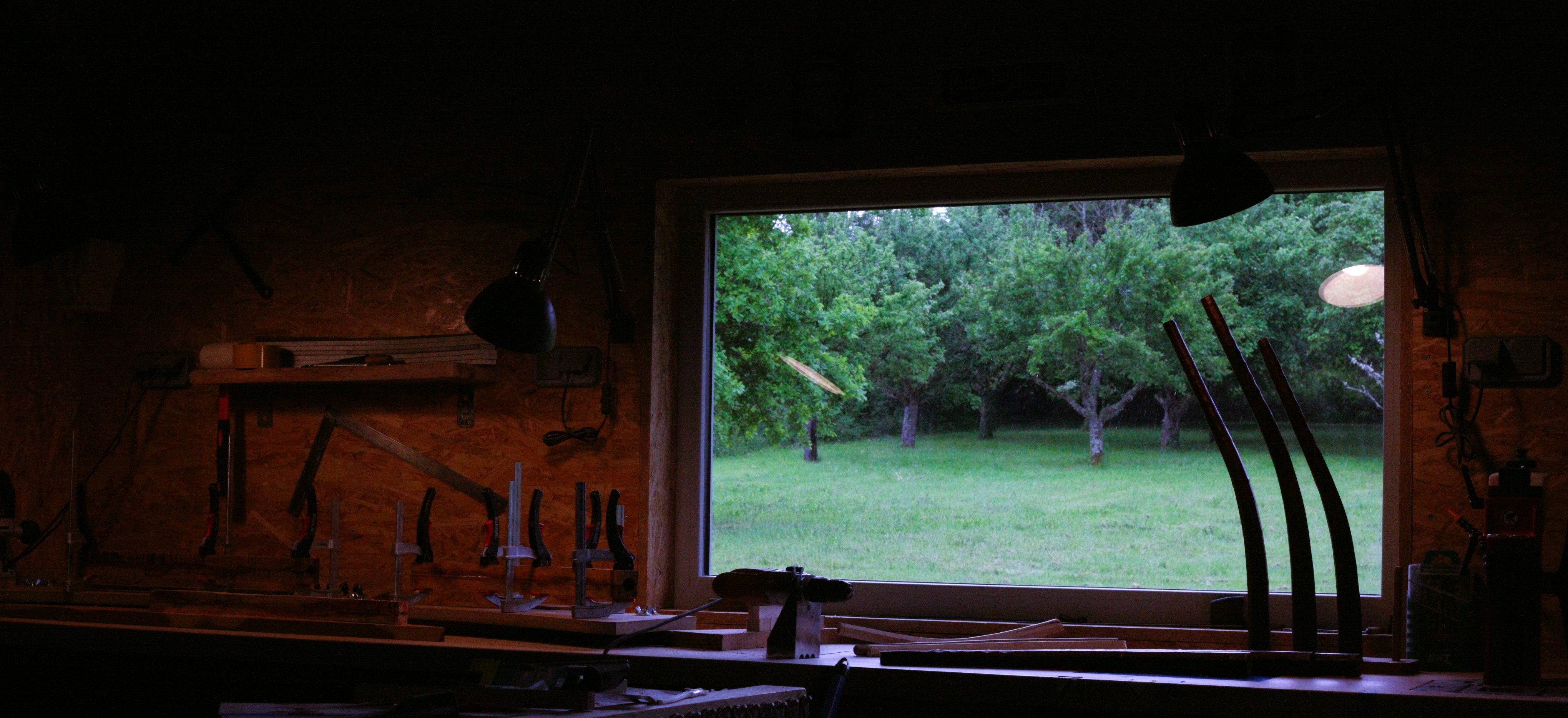 Intérieur de l'atelier Tinctoris — Manufacture Delmas : fenêtre donnant sur la nature, outils accrochés au mur de briques, cornets à bouquin en silhouette
